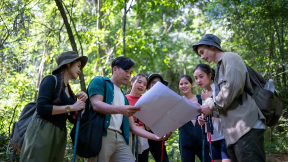 Sechs Jugendliche sind auf einer Exkursion im Wald. Sie halten und betrachten zusammen einen Plan.
