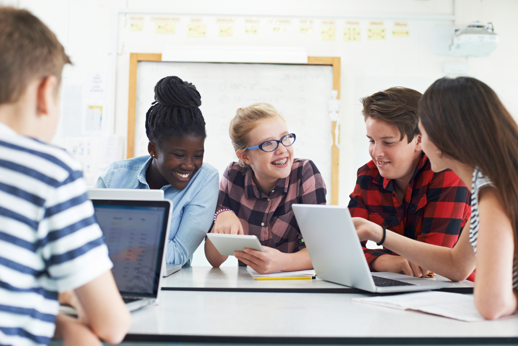 Mehrer Schüler sitzen vor Laptops/Tablets und unterhalten sich.